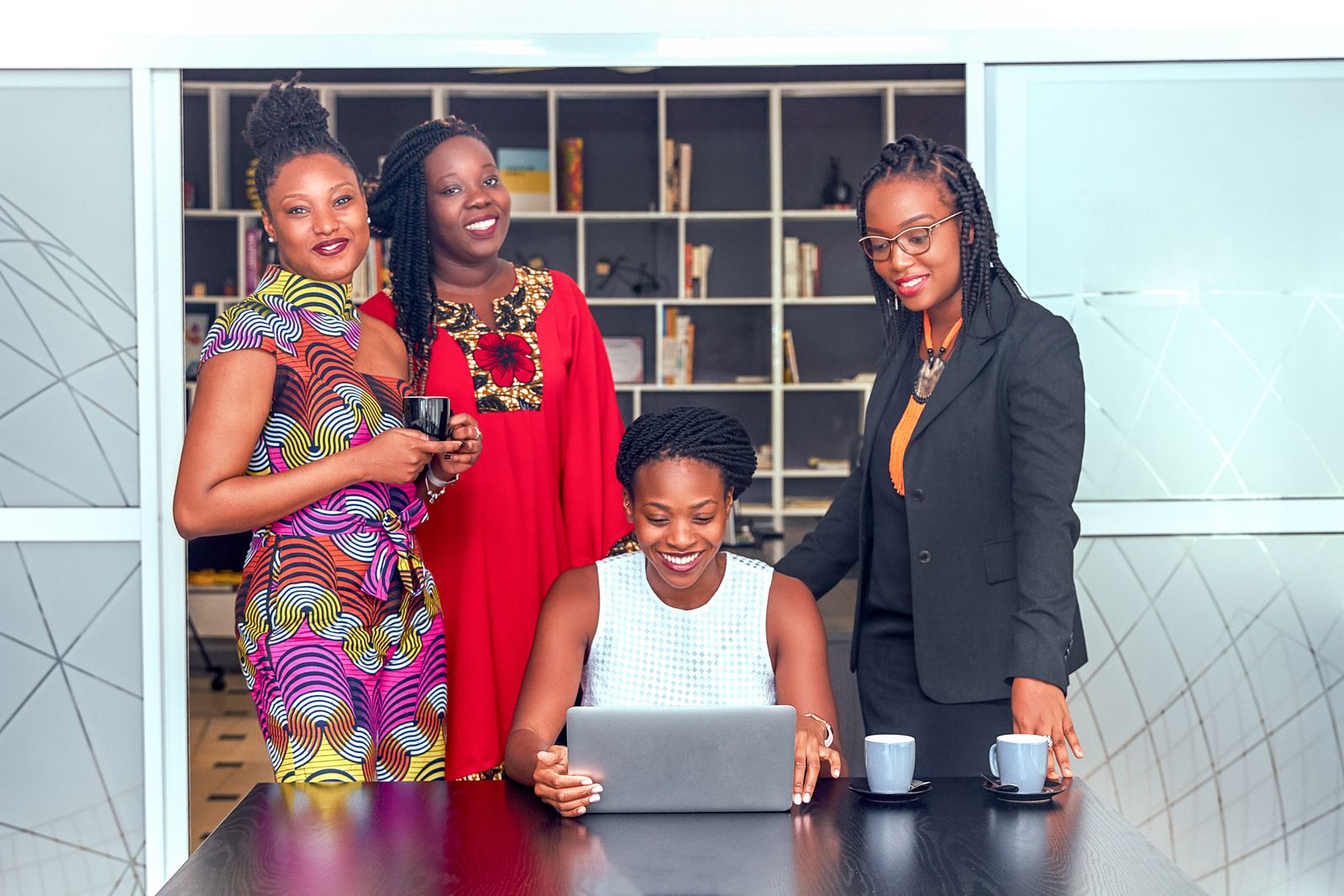 Four women working together around a laptop in an office