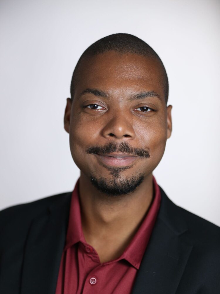 Portrait of a smiling man with a moustache in a dark blazer and maroon shirt