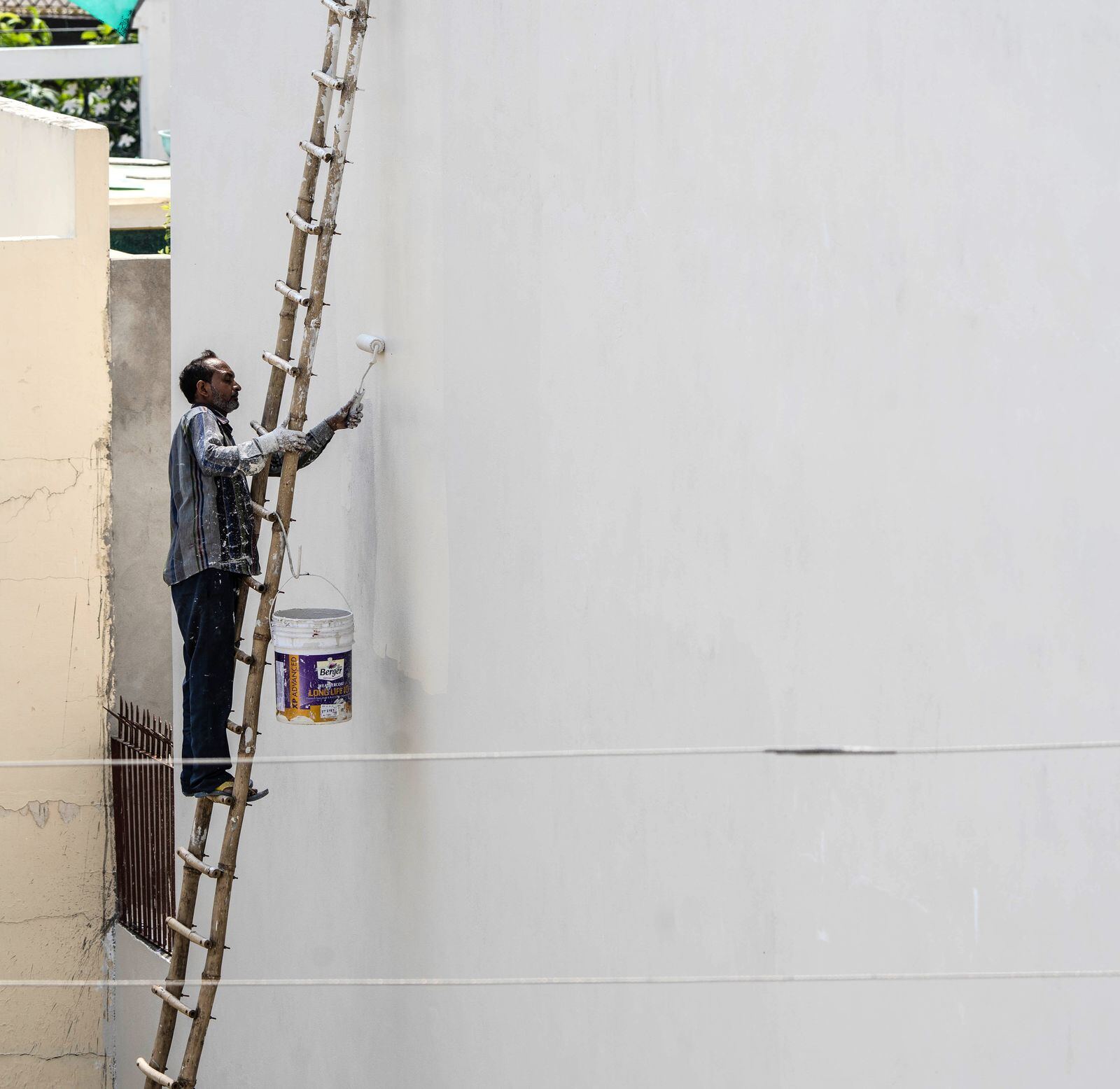 Painter on a ladder painting an exterior wall with a roller